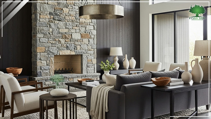 اتاق نشیمن معاصر با دیوار سنگی شومینه و دیوارکوب چوبی تیره. مبلمان تیره، میزهای کنارمبلی گرد، و لوستر استوانهای فلزی بزرگ.